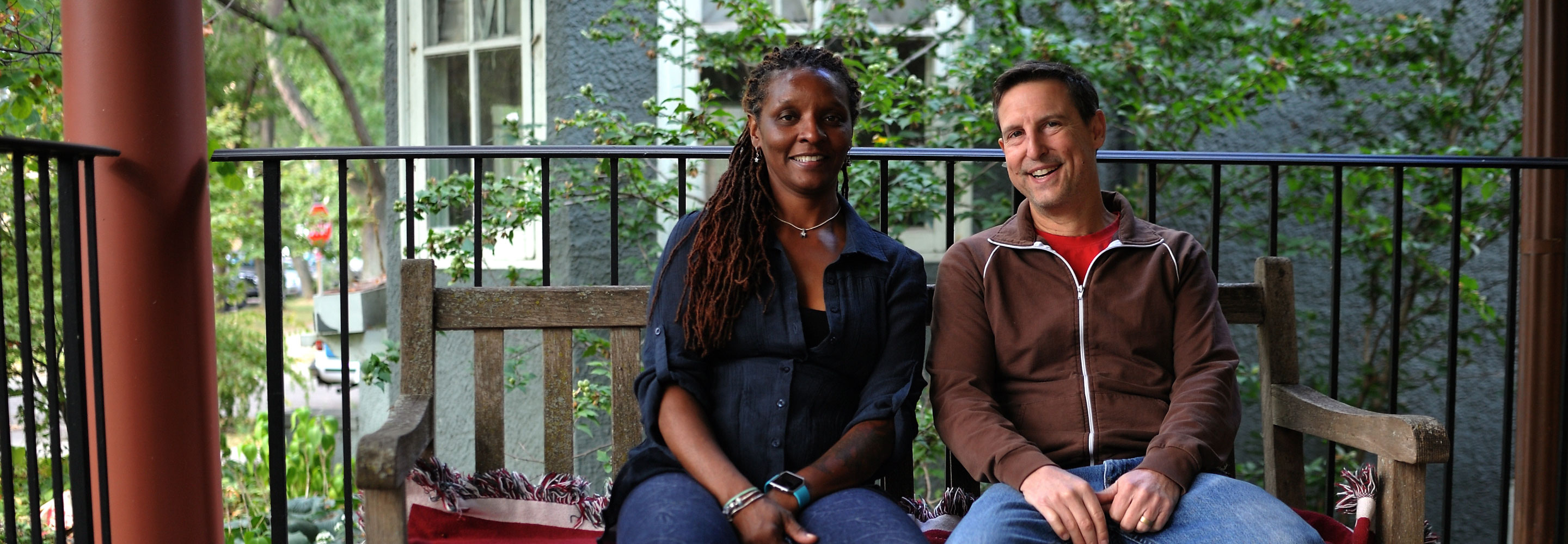 Two people sitting on a bench on their front porch.