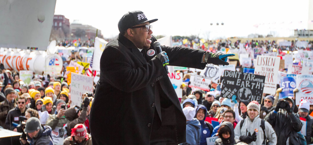 A man speaks into a microphone in front of a crowd of people.