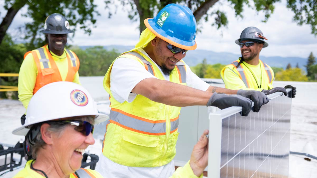 Four people, dressed in hard hats and fluorescent vests, working on a solar panel