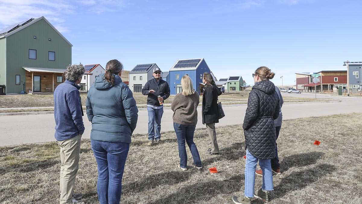 a group of people are gathered around a man who is speaking to them, the are outside