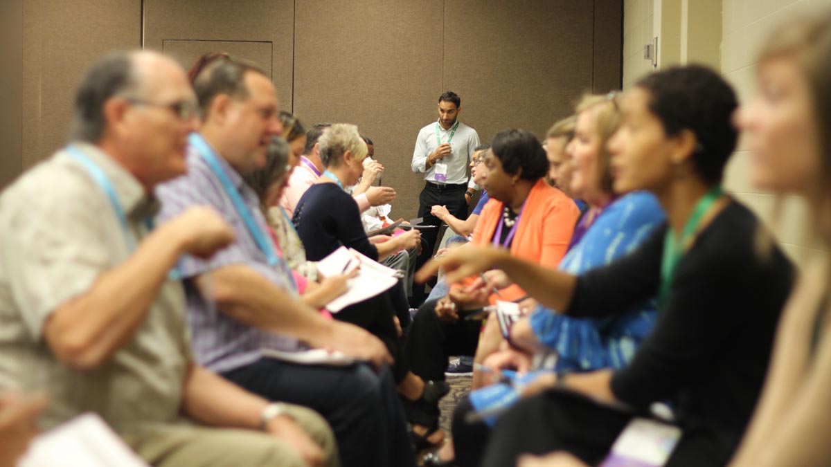 A diverse group of individuals seated in chairs, engaged in discussion at a professional conference setting.