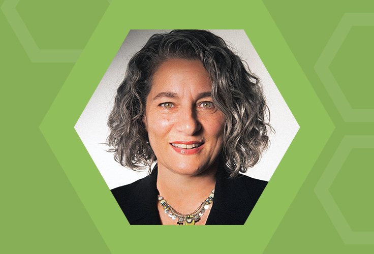 Headshot of a woman with curly gray hair, wearing a black blazer and a colorful necklace.