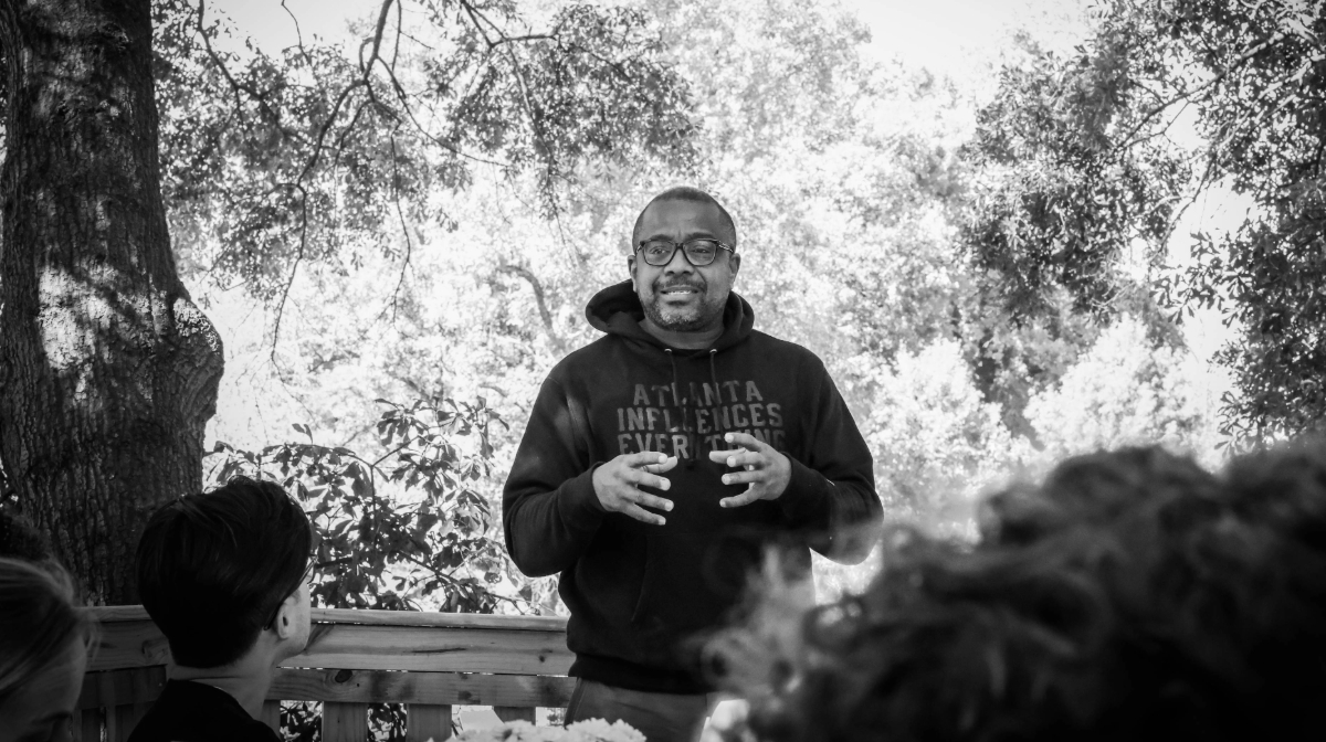 A man in a hoodie speaking passionately in front of a group of people. 