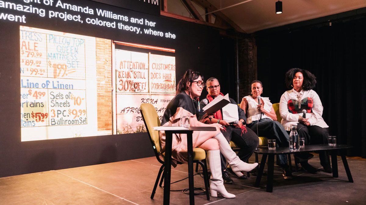 A quartet of women sit in a row of chairs for a panel discussion. Each woman holds a microphone.