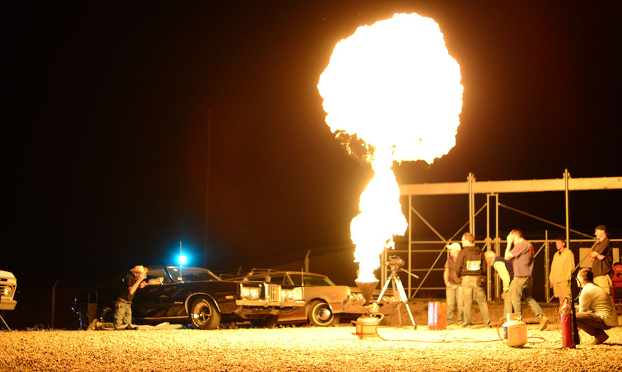 night photo of a flame plume and men standing around it