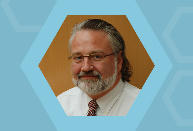 A man with a gray beard and glasses wearing a white shirt and tie.