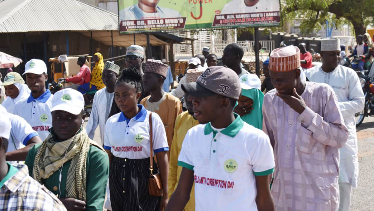 A group of people walking on a street, some wearing white T-shirts with logos.