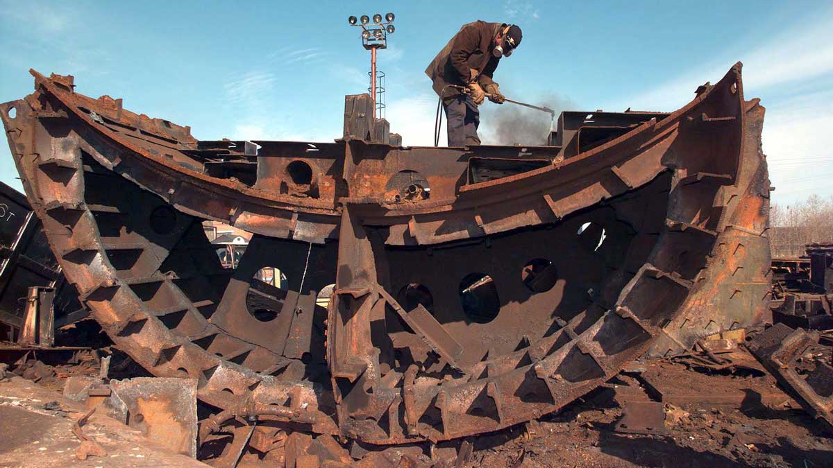 A person using a wielding torch to disassembling a rusty old Soviet Oscar-class submarine.