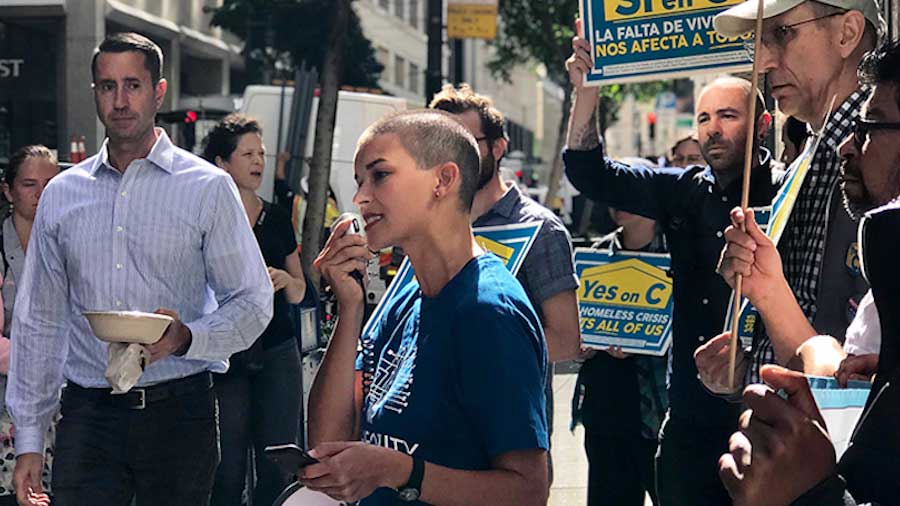 a woman on the sidewalk speaking to passerbys through a loud speaker