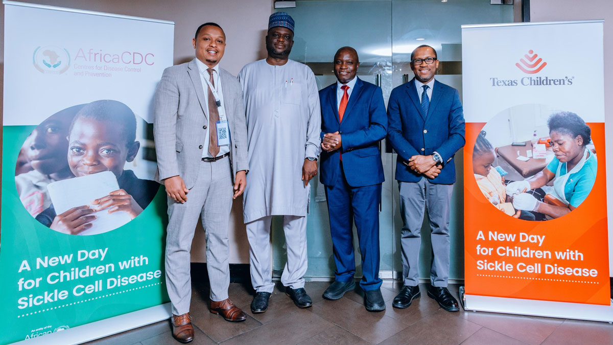 Four men in formal wear stand between banners promoting sickle cell disease awareness.