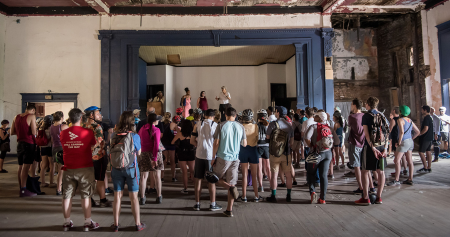 Crowd_Of_People_In_Dilapidated_Theater_Space_Listening_To_Person_On_Stage